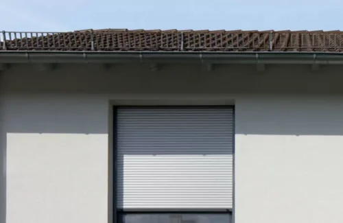 Ein Rolladen in einer hell angestrichenen Hausfassade schützt den Innenraum vor starker Sonne.