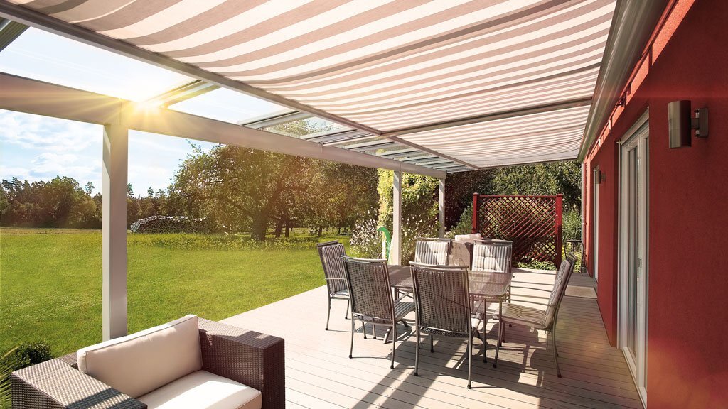 Ein gläsernes Terrassendach mit Glaseinsätzen, unter denen eine Wintergarten-Markise mit gestreiftem Tuch hängt.