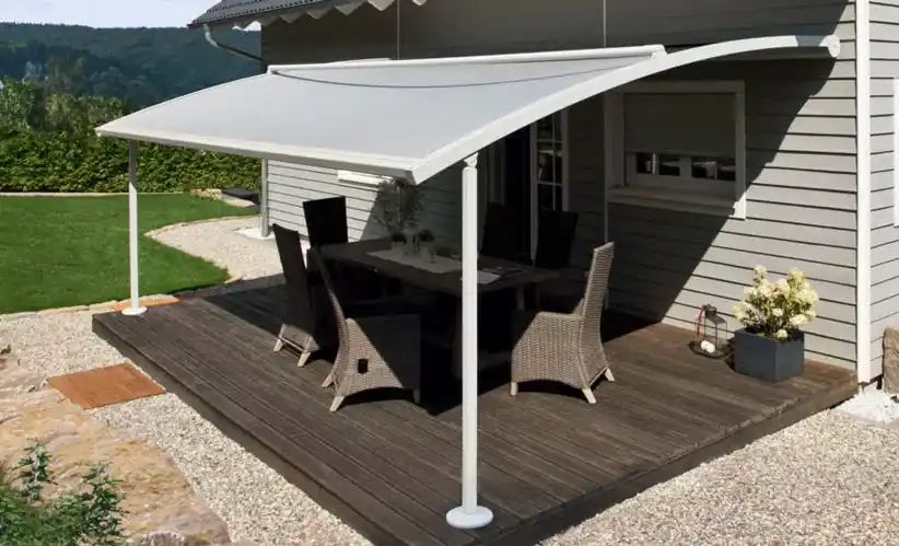 Gebogenes Glasvordach mit aufliegender Markise über Holzterrasse mit Sitzmöbeln.