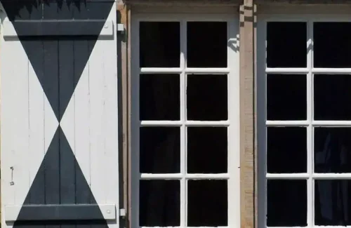 Fenster mit weiß-grau gemustertem Klappladen an der Seite.