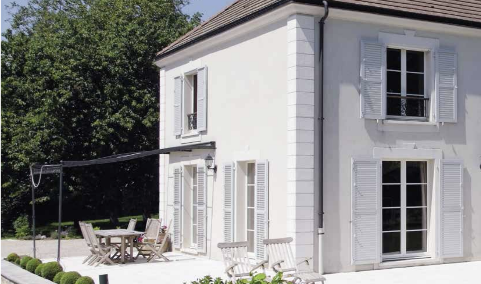 Ein helles Haus mit mehreren weißen Klappläden an den Fenstern